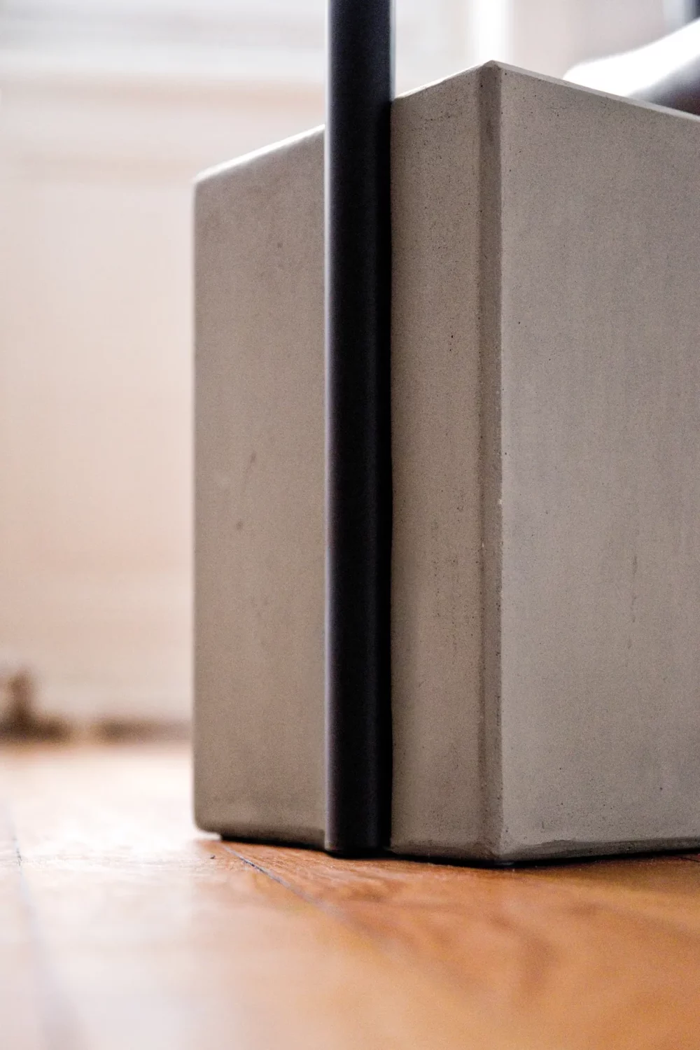 Close-up on the opposition between the smooth finish of the black paint and the assumed texture of the fibered concrete that constitutes the ballast of the pedestal table